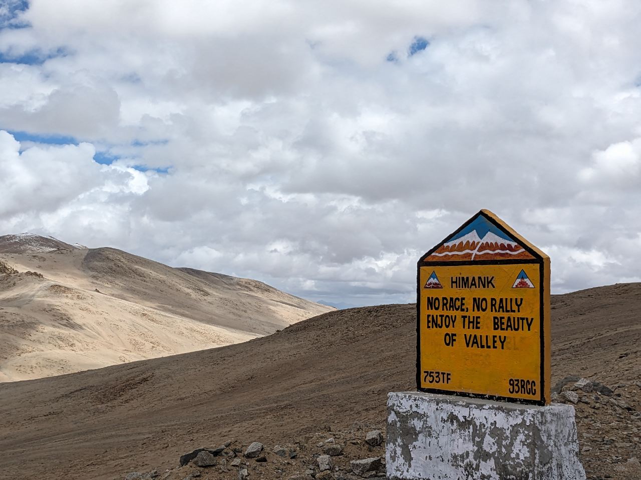 A painted yellow Himank Border Roads milestone reading 'No race, no rally — enjoy the beauty of valley'.